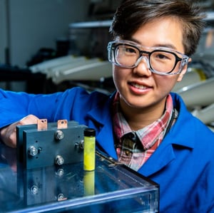 Photo of flow battery researcher Ruozhu Feng posing with ingredients for a long-lasting grid energy battery