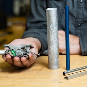 Photo of a person holding a pile of aluminum scrap next to four cylinders of recycled aluminum scrap