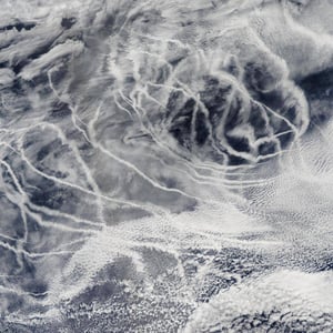 This aerial image depicts a portion of Earth's surface where typical white clouds are interspersed with thin, linear clouds that designate maritime shipping routes.
