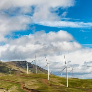 Photo of a hillside with wind turbines against a blue sky.