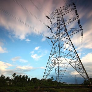 Photograph shows a transmission tower against a blue, cloudy sky.