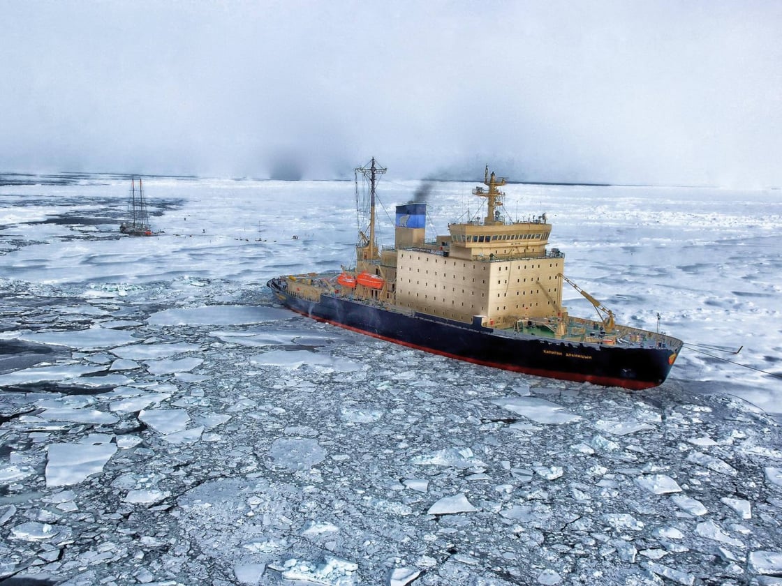 Photograph shows a large ship sailing through ice-covered waters.